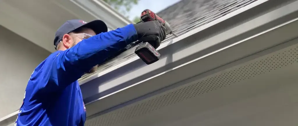 Person using a drill on a houses gutter Person using a drill on a house's gutter