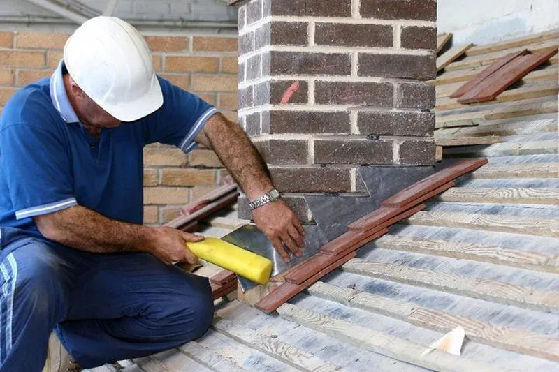 Man installing roofing tiles near a chimney Man installing roofing tiles near a chimney