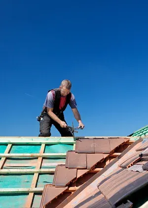 Man installing tiles on a roof under clear blue sky