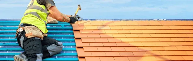 Worker installing roofing tiles on a sloped roof
