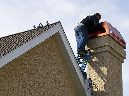 A worker on a ladder repairs a chimney cap atop a house A worker on a ladder repairs a chimney cap atop a house