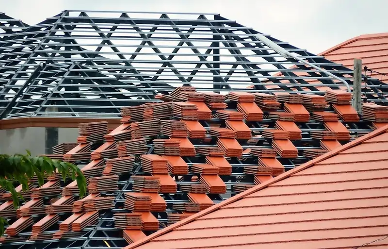 Close up of stacked orange roof tiles beside a partially constructed black metal frame roof Close up of stacked orange roof tiles beside a partially constructed black metal frame roof
