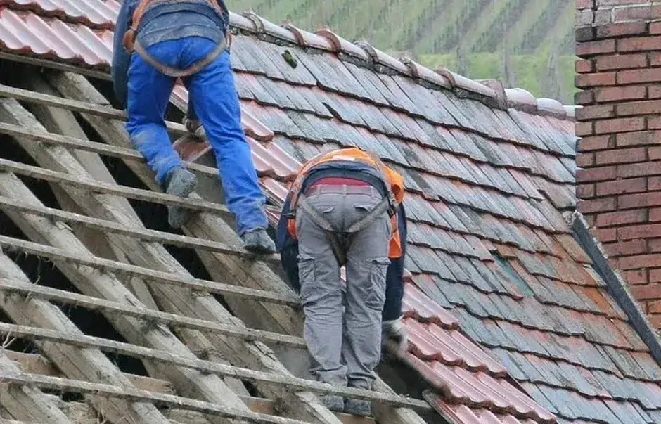 Two roofers in safety harnesses are working on a sloped roof Two roofers in safety harnesses are working on a sloped roof