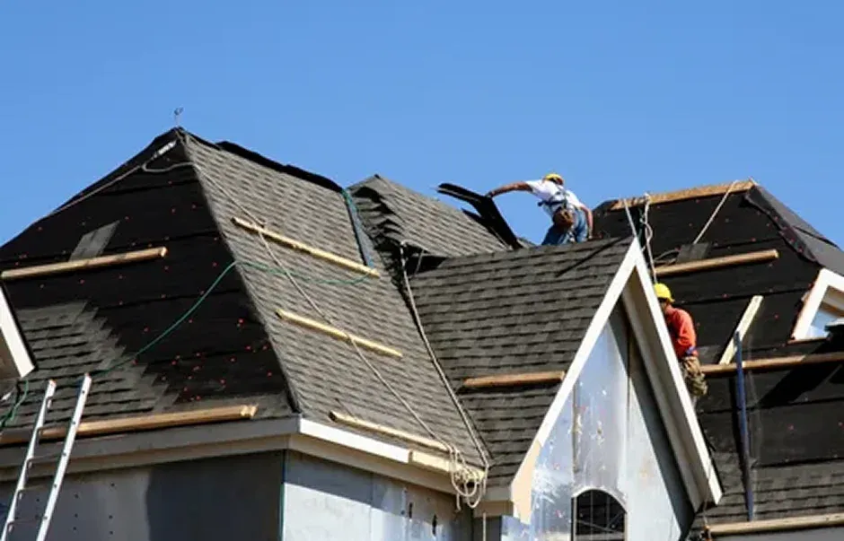 Two roofers work on a house roof under a clear blue sky Two roofers work on a house roof under a clear blue sky