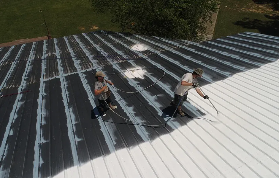 Two workers spray painting a metal roof one on the left applying a white coat Two workers spray painting a metal roof, one on the left applying a white coat